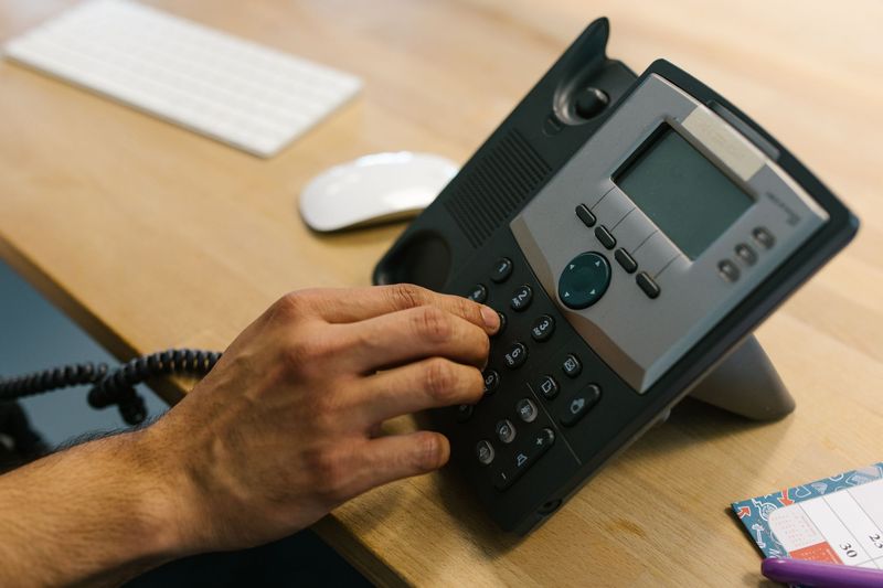 Hand wählt eine Nummer auf einem Bürotelefon