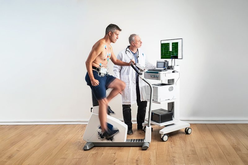 Patient auf dem Ergometer, der Arzt verfolgt das Belastungs-EKG am Wagen