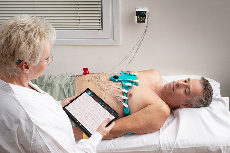 Patient liegt mit angelegtem EKG-Gürtel, die Ärztin liest das Ruhe-EKG am Tablet